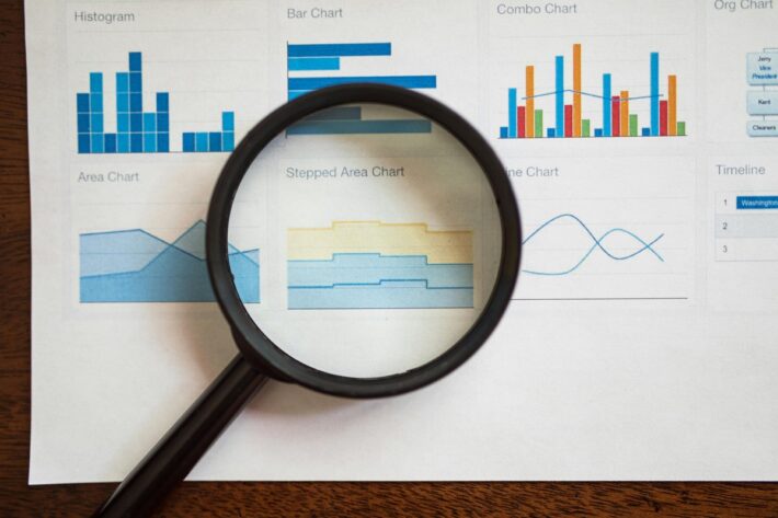 Magnifying glass over printed charts, comparing reports when choosing help desk software